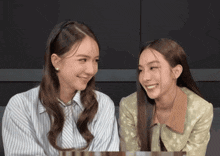 two women are looking at each other and smiling while sitting next to each other