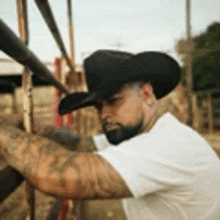 a man with a beard wearing a cowboy hat and a white shirt is standing in front of a fence .