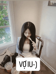 a woman sits at a table with a spoon in her mouth and a sign that says vo iu- )