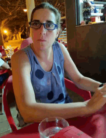 a woman wearing glasses sits at a table with a glass of water in front of her