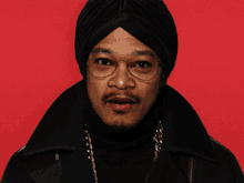 a man wearing glasses and a turban says wow in front of a red background