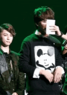 a man wearing a mickey mouse sweater is covering his face with a piece of paper