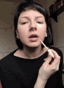 a woman with a nose ring is applying concealer