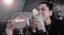 a woman is drinking a drink with a slice of lemon on it .