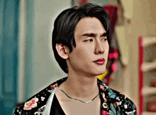 a young man is wearing a floral shirt and a necklace .
