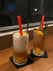 two drinks with orange straws sit on a table