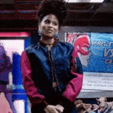 a woman wearing a blue and pink jacket is standing in front of a sign that says ' wrestling vs ' .