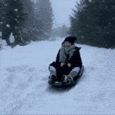 a woman sledding down a snowy hill with trees in the background