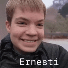 a young man is smiling and wearing a black jacket with the name ernesti written on it .