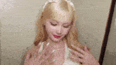 a woman with long blonde hair and long nails is wearing a white dress and a headband .