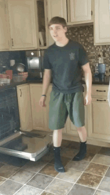 a young man in a black shirt stands in a kitchen