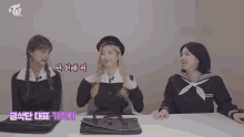 three girls in school uniforms are sitting at a table with a briefcase