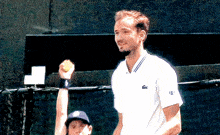 a man in a white shirt with a lacoste logo on the sleeve holds a tennis ball