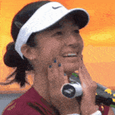 a woman wearing a nike hat is smiling and holding a tennis racket