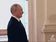 a man in a suit and tie is standing in front of a window and smiling .