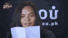 a woman is holding a piece of paper in front of a sign that says oi ou.ph