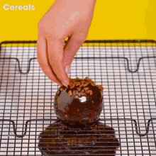 a person is decorating a chocolate donut with cereal sprinkles