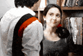 a man and a woman are looking at each other in front of a book shelf