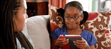 a girl wearing glasses is sitting on a couch holding a tablet