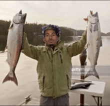 a man in a green jacket is holding up two fish
