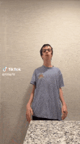 a boy wearing glasses and a blue shirt is standing in front of a counter with tiktok written on the bottom right