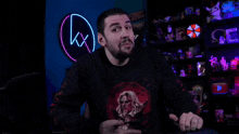 a man with a beard is talking in front of a neon sign that says kx