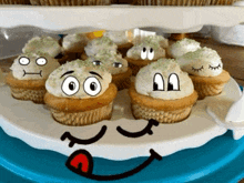 a tray of cupcakes with faces drawn on them on a blue plate .