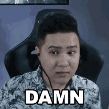 a man wearing headphones is sitting in a chair with the word damn on his face .