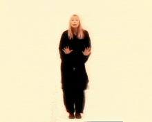 a woman in a black coat is standing in front of a yellow background