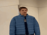 a young man wearing a blue jacket is standing in front of a wall .