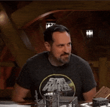 a man wearing a black star wars t-shirt is sitting at a table