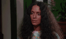 a woman with long curly hair is wearing a pink shirt