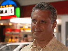 a man in a plaid shirt is smiling in front of a sign that says mais