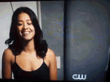 a woman in a black tank top is smiling in front of a screen that says cw .