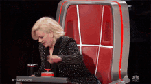 a woman is sitting in a red chair with a nbc logo on the back