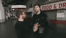 a couple of men are standing next to each other in front of a food and drink stand .