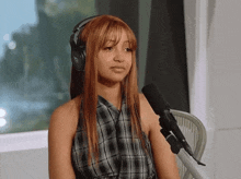 a woman wearing headphones and a plaid shirt is sitting in front of a microphone with the letter b on it
