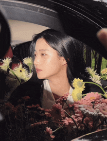 a woman is sitting in a car surrounded by pink and yellow flowers