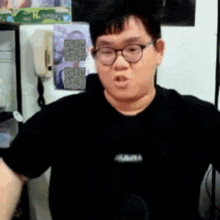 a man wearing glasses and a black shirt is talking into a microphone in a room