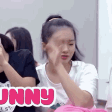 a girl is sitting in front of a group of people and covering her eyes with her hands .
