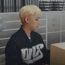 a man wearing a black and white striped shirt with the letter t on it sits in front of a filing cabinet