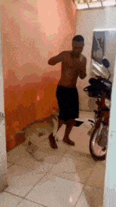 a shirtless man is standing next to a dog in a room with a motorcycle in the background .