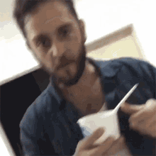 a man with a beard is holding a cup of yogurt and a spoon in his hand .