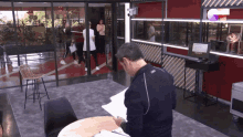 a man sits at a table in front of a sign that says g on it