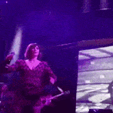 a woman is playing a guitar and singing into a microphone on a stage in front of a large screen .