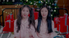 two girls are sitting next to each other in front of a christmas tree and gifts
