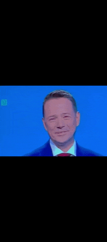 a man in a suit and tie is smiling while standing in front of a blue background .
