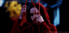 a woman in a red hood is holding a red string in her hand .