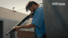 a man in a blue shirt holds a shotgun in front of a sign that says countdown
