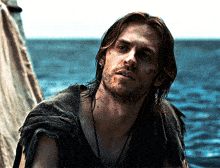 a man with long hair and a beard is standing in front of a body of water